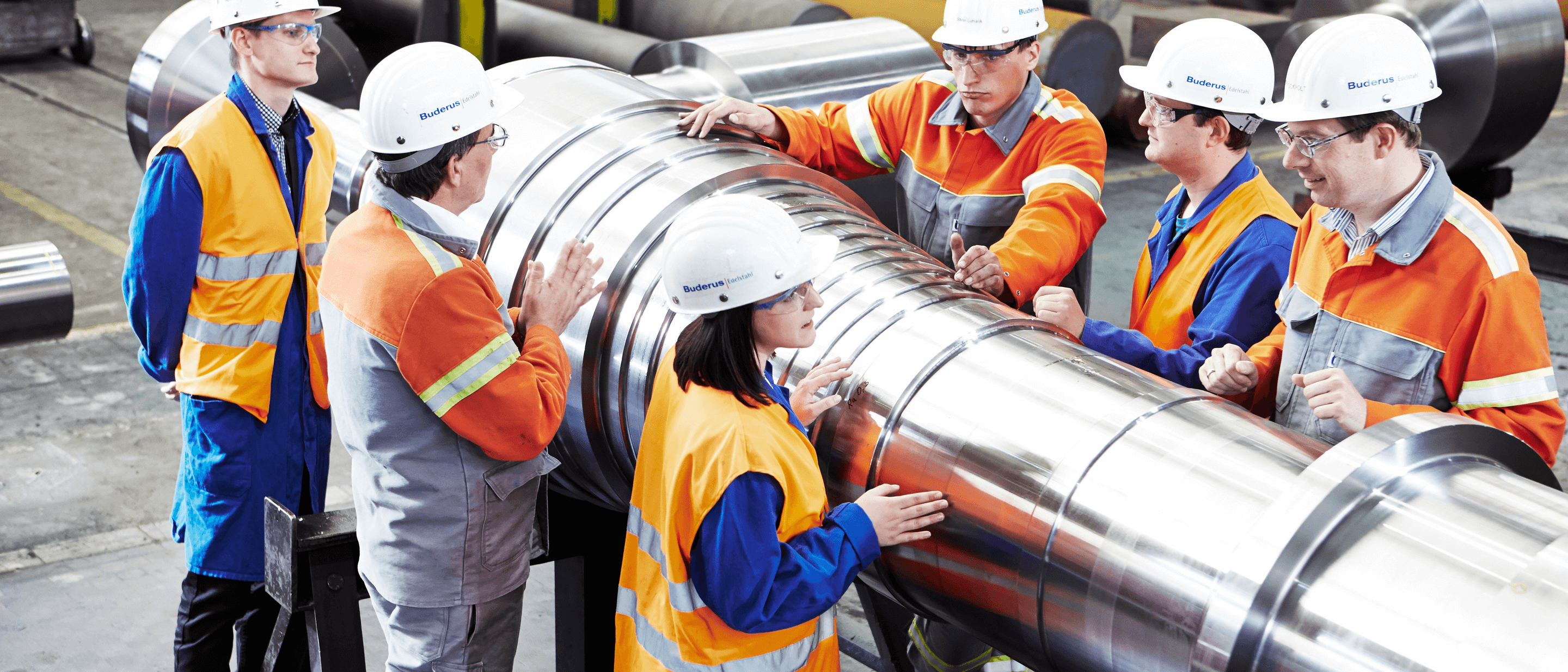 fünf Arbeiter die Schutzkleidung tragen und in der Freiformschmiede arbeiten.